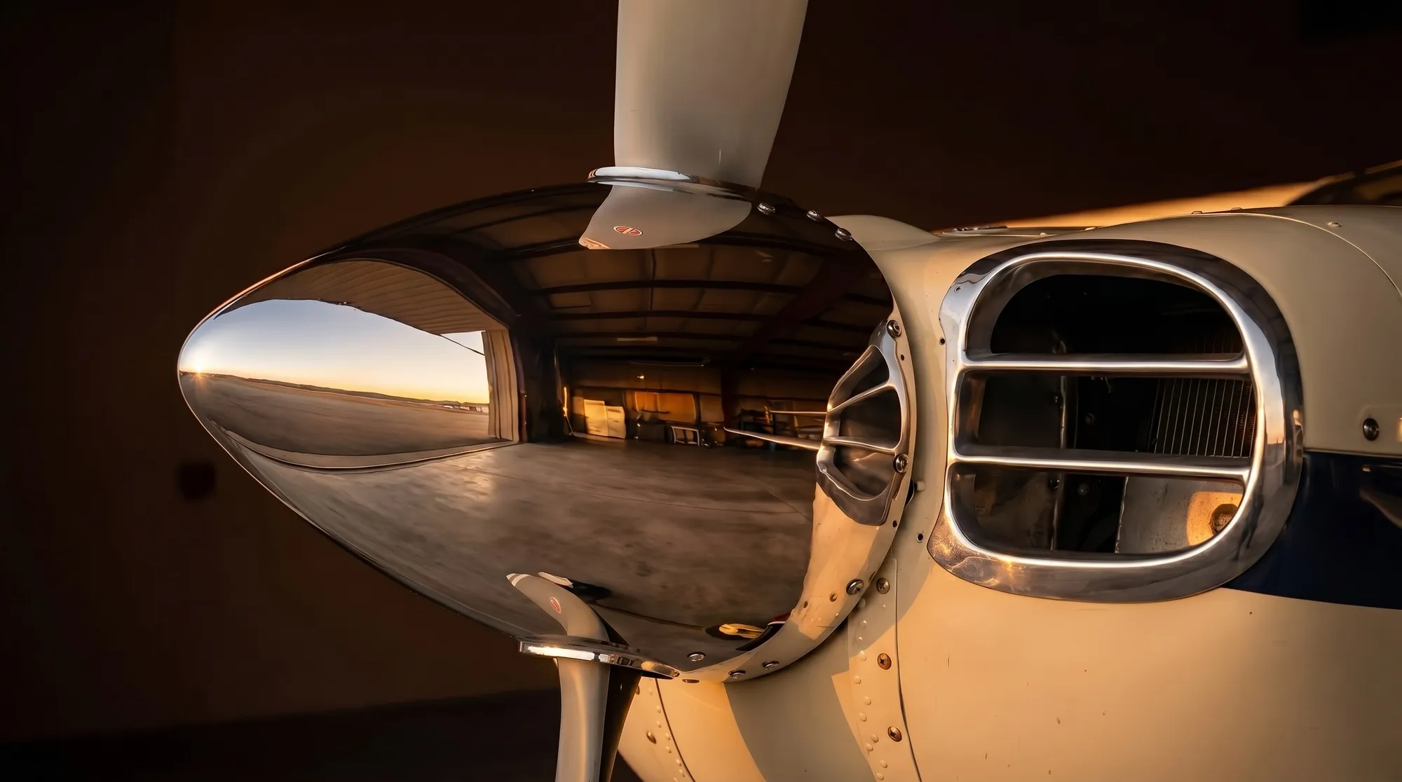Mirror-polished aircraft spinner and cowl reflecting the hangar at golden hour